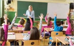 A classroom of students raise their hands to ask a question