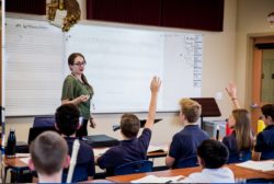 Female teacher in front of class with hands raised