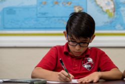 male student writing in front of a map