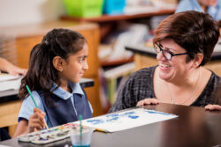 Adult smiling at a student working on an art project