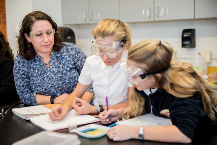 Science teacher wearing goggles with two students