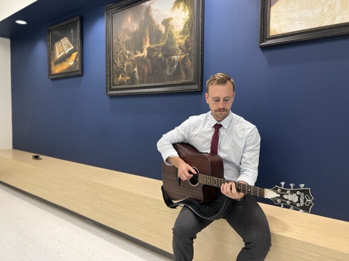 Stuart Coles, music teacher at Great Hearts Harveston, playing a guitar in hallway.