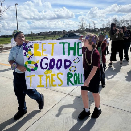 Students at Great Hearts Harveston Mardi Gras parade holding banner.