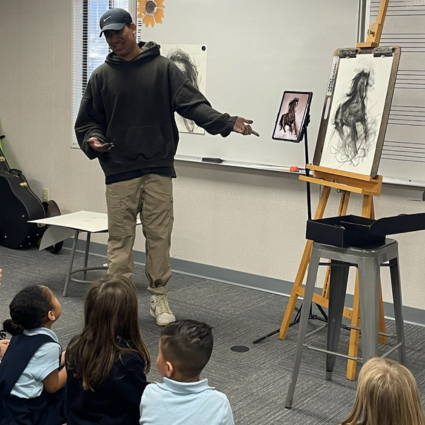 Charcoal artist speaking to students next to his artwork