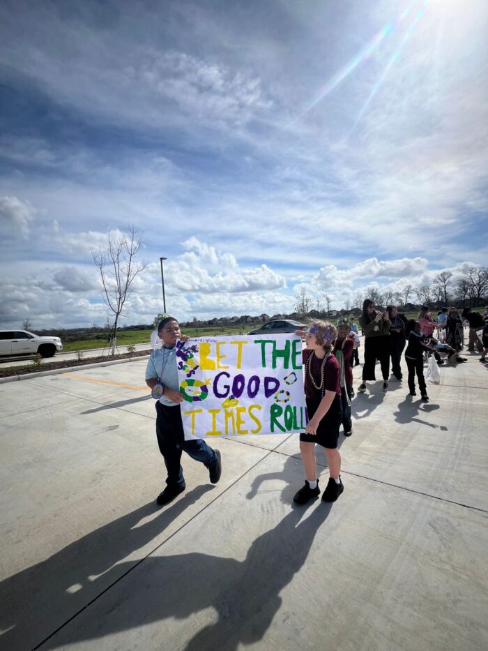 Students at Great Hearts Harveston Mardi Gras parade holding banner.