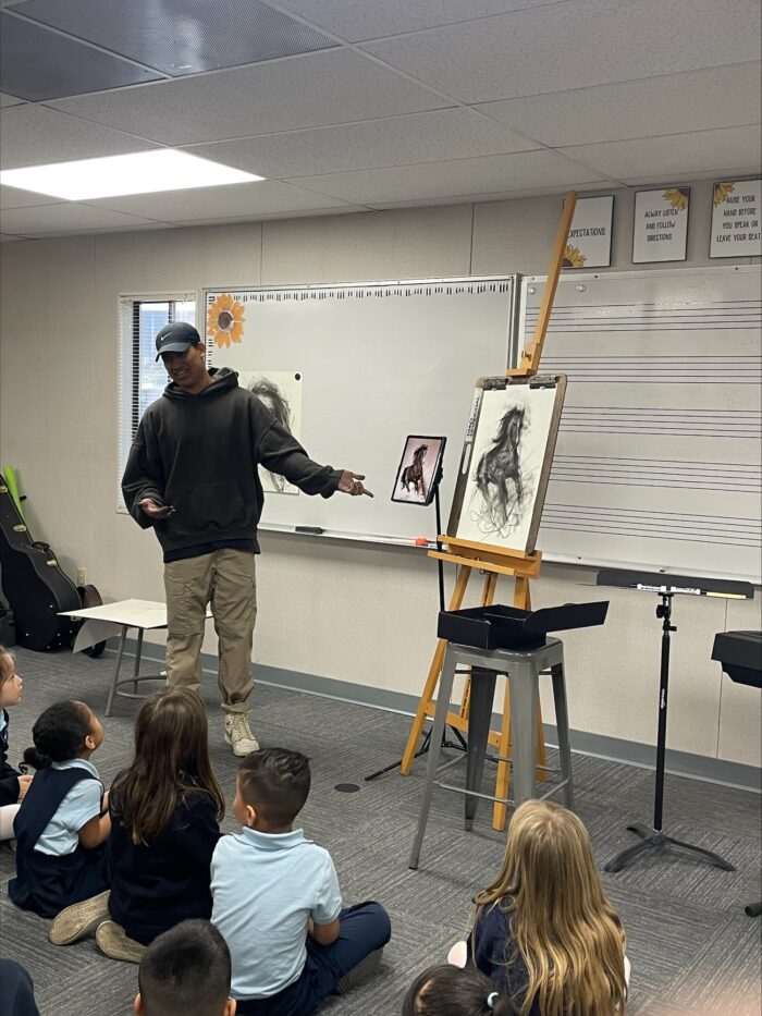 Charcoal artist speaking to students next to his artwork