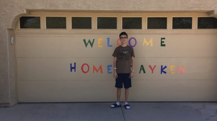 Jaken Beal in front of garage door with welcome home sign
