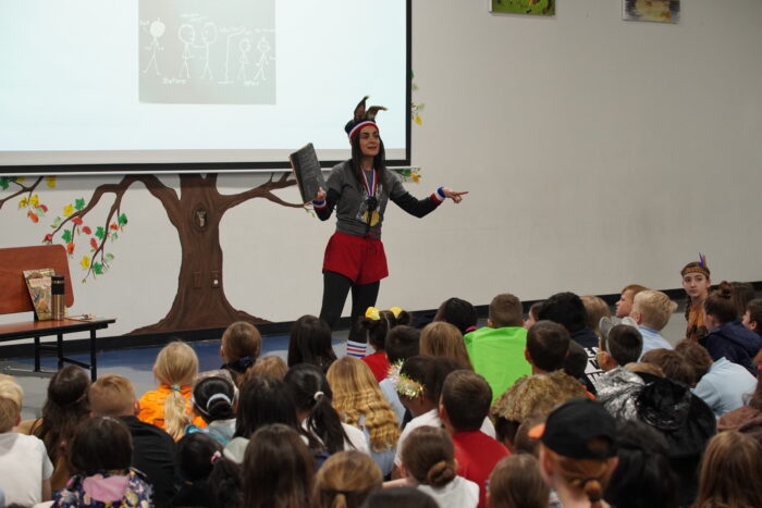 Headmaster dressed as literary character reading to assembly of students