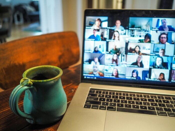 A laptop with a zoom call on the screen and a ceremic mug next to it on a table
