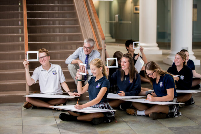 A group of students sitting on the floor working on a pencil sketch projects.