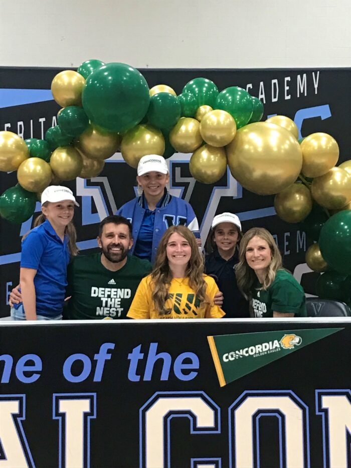 Student-athlete posing with family at college commitment signing ceremony.