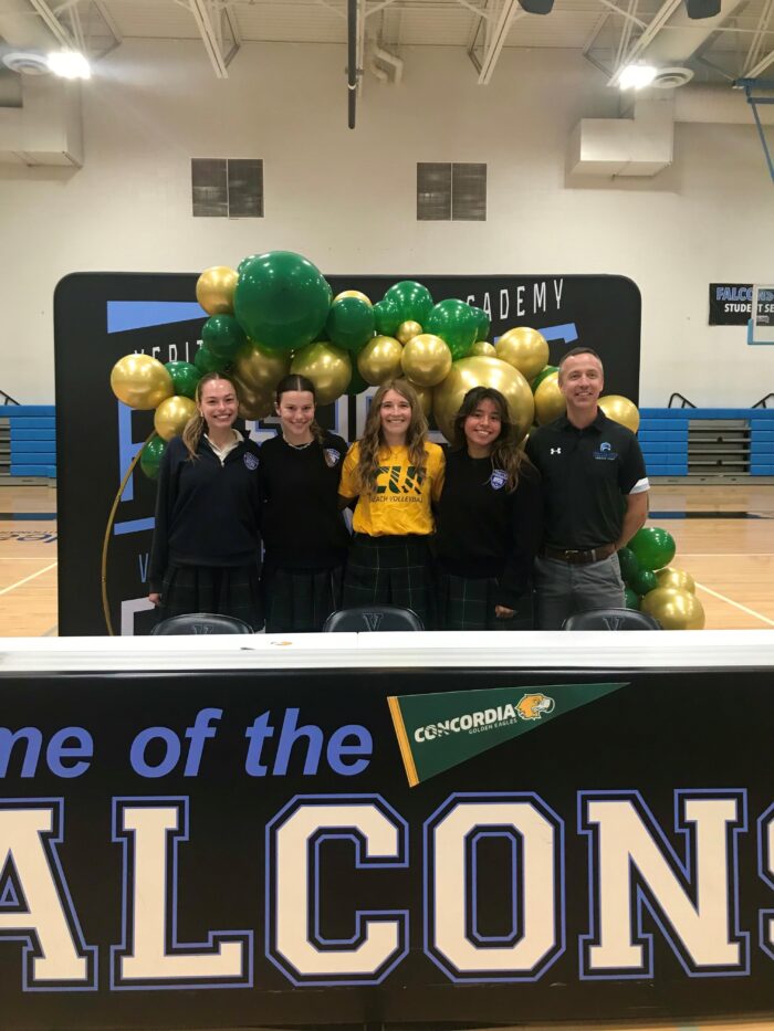 Student-athlete posing with friends and coaches at college commitment signing ceremony.