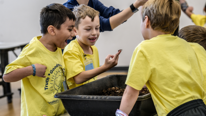 Three boys existed about a worm that one of them is holding.