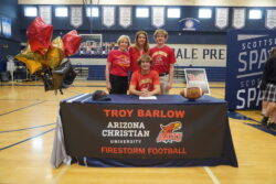Student athlete posing with his family and ACU banner