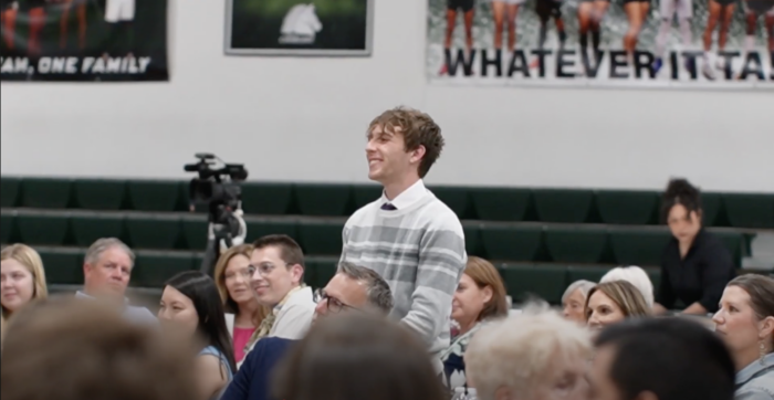 Student standing in a crowd of seated people