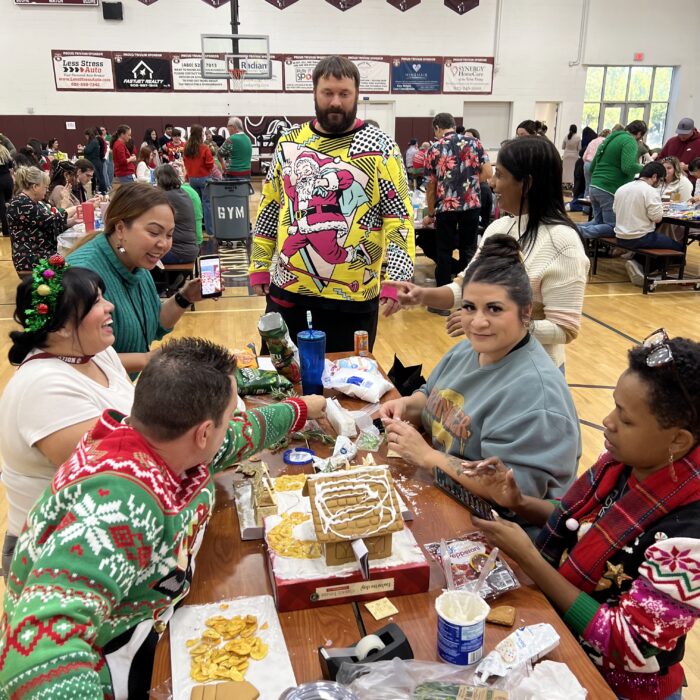 team with holiday sweaters and gingerbread house