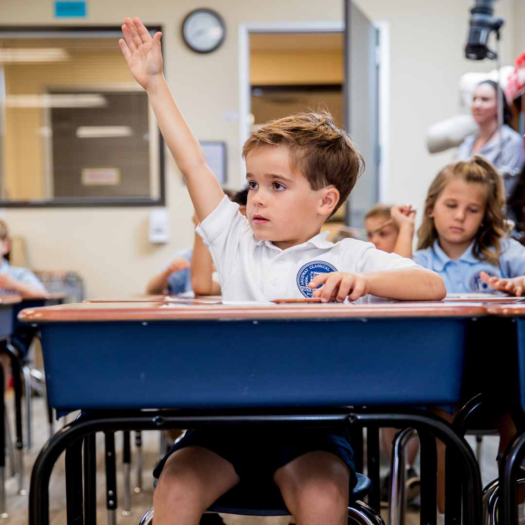 Kindergarten student raising his hand at his desk